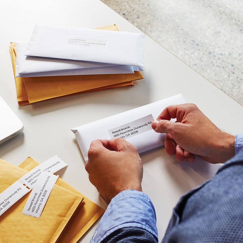 Person writing and organising paperwork with address labels on a desk