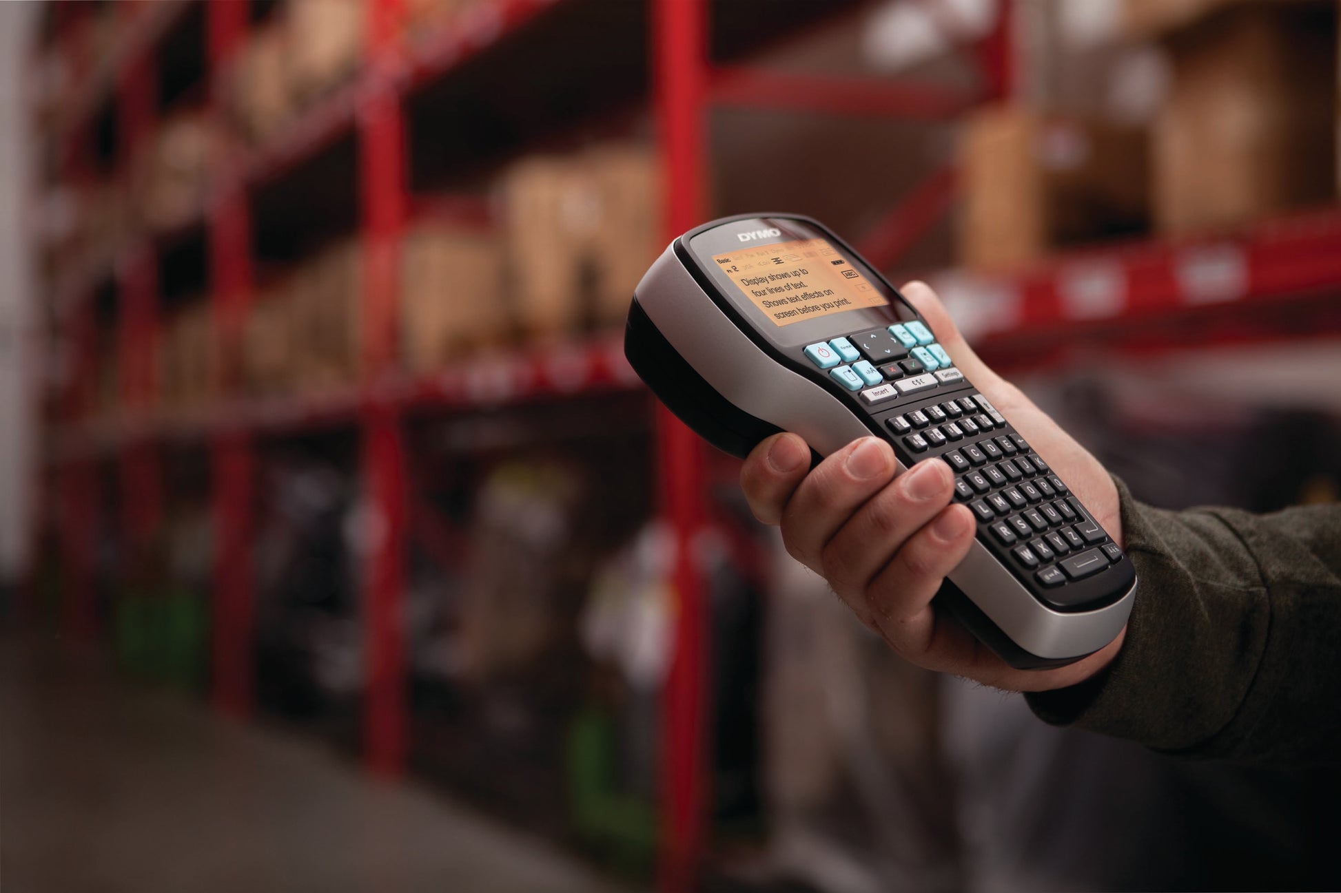 Person holding a DYMO LabelManager 420P in a warehouse aisle for portable shelf and stock labelling