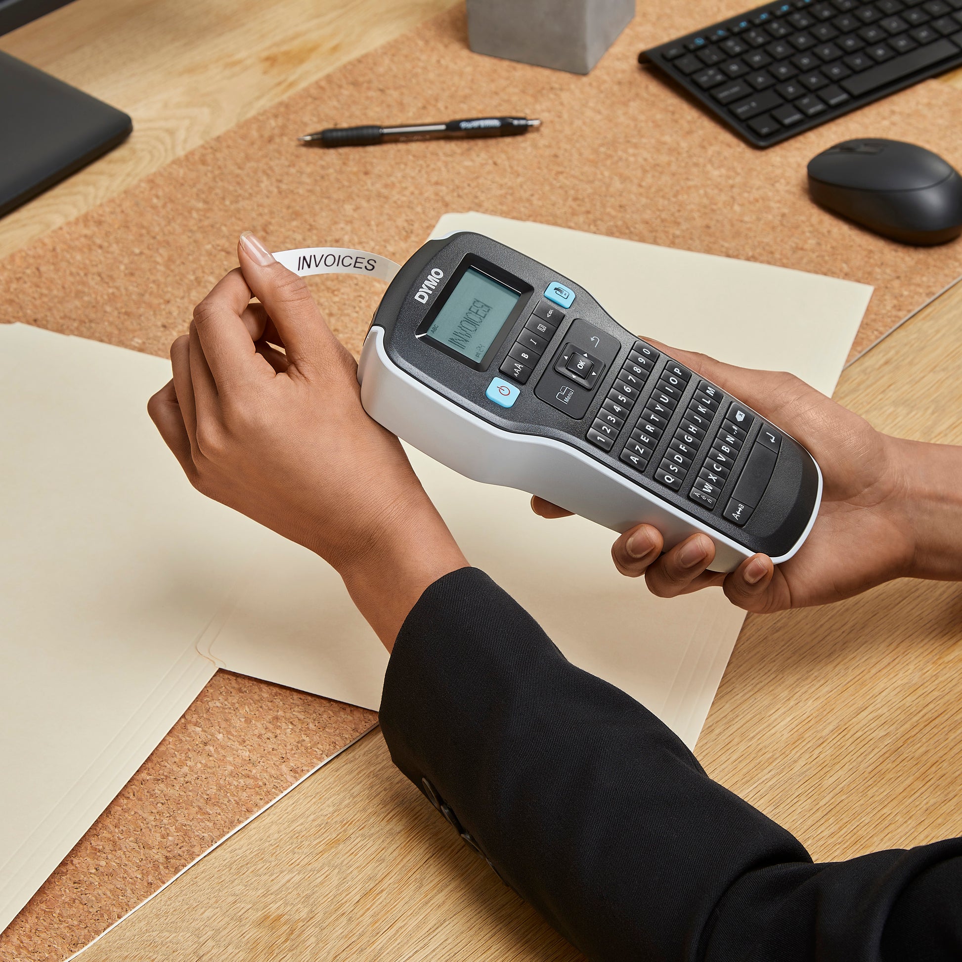 Person holding a Dymo LabelManager label maker at a desk