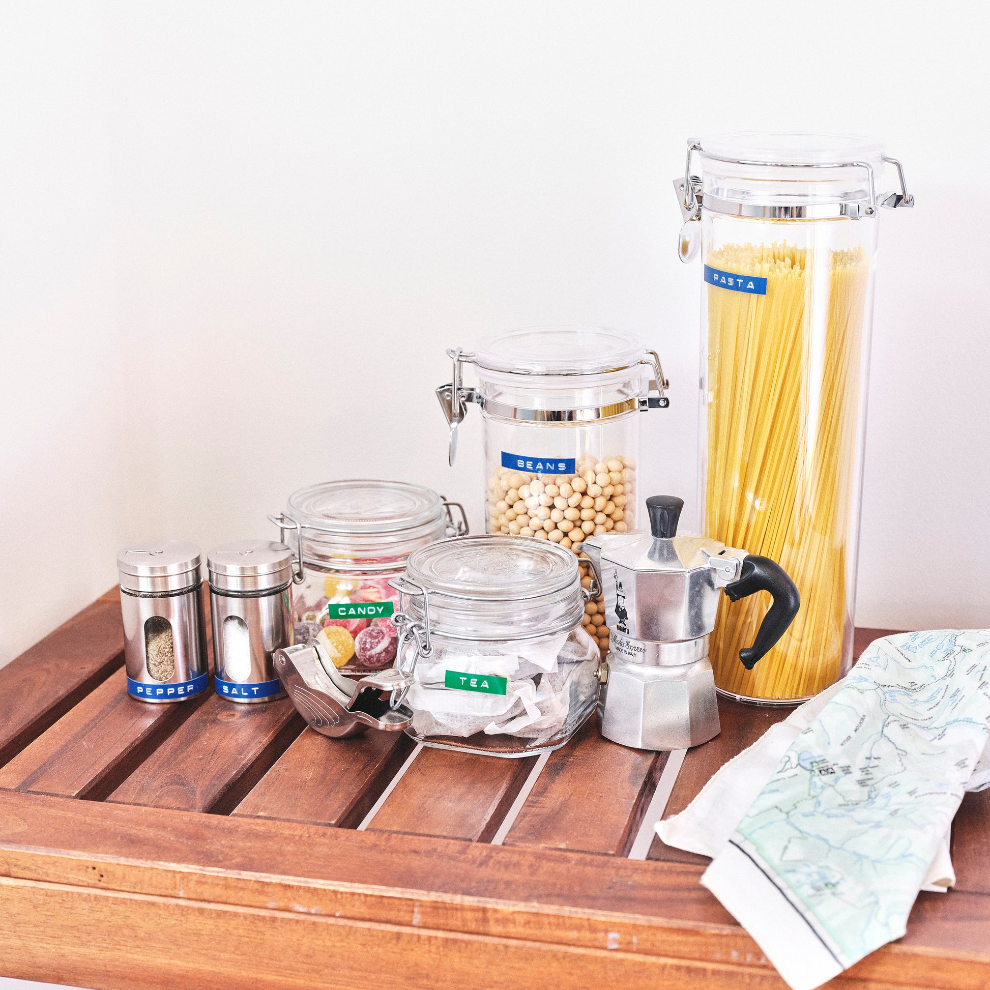 Labelled kitchen jars and canisters for pasta, beans, tea, candy, salt and pepper on a wooden bench