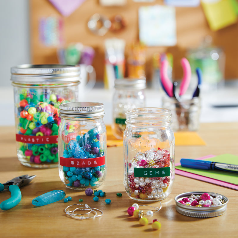 Decorative jars and containers labelled with colourful embossed tape on a craft table