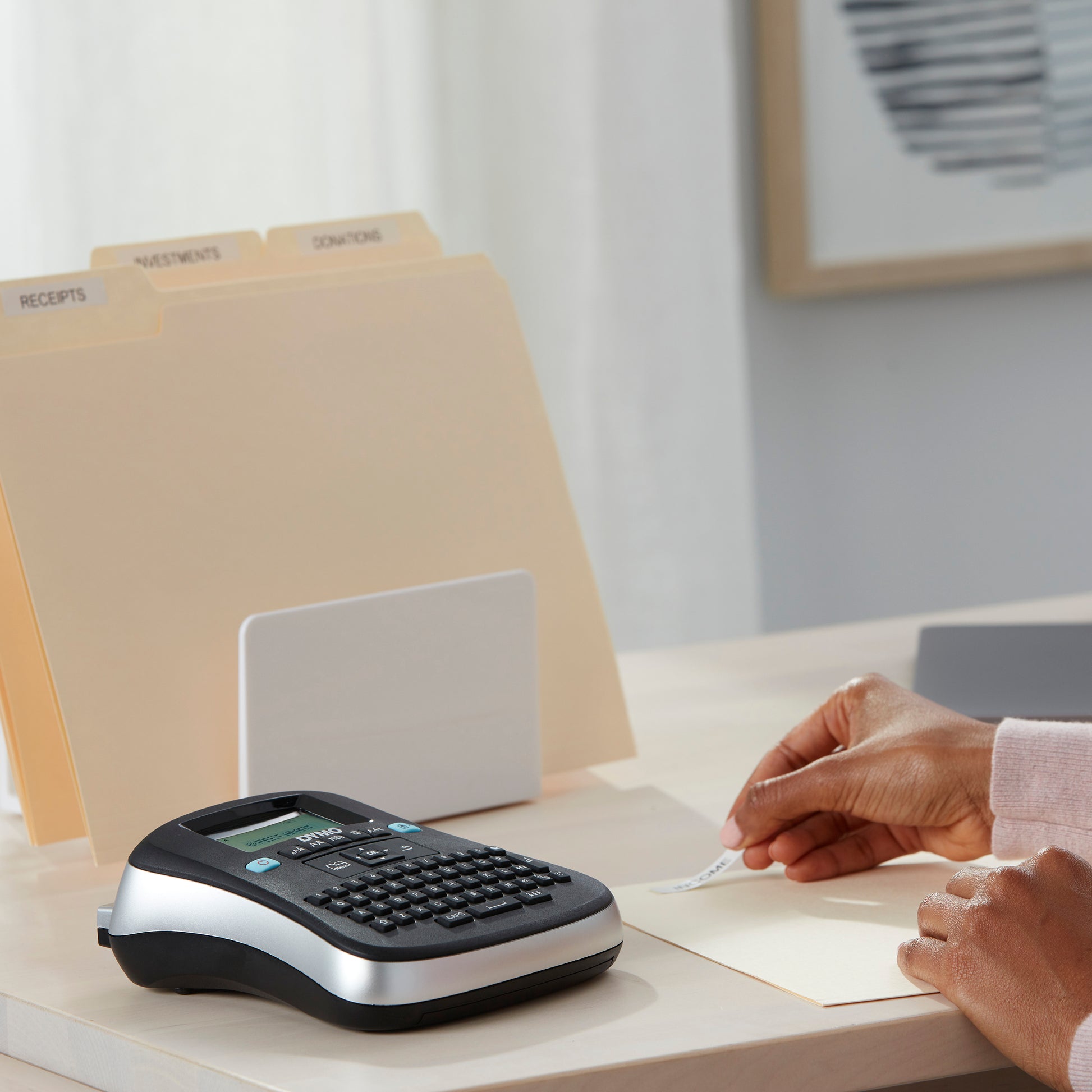 DYMO desktop label maker beside labelled file folders while a printed label is applied for home office document organisation