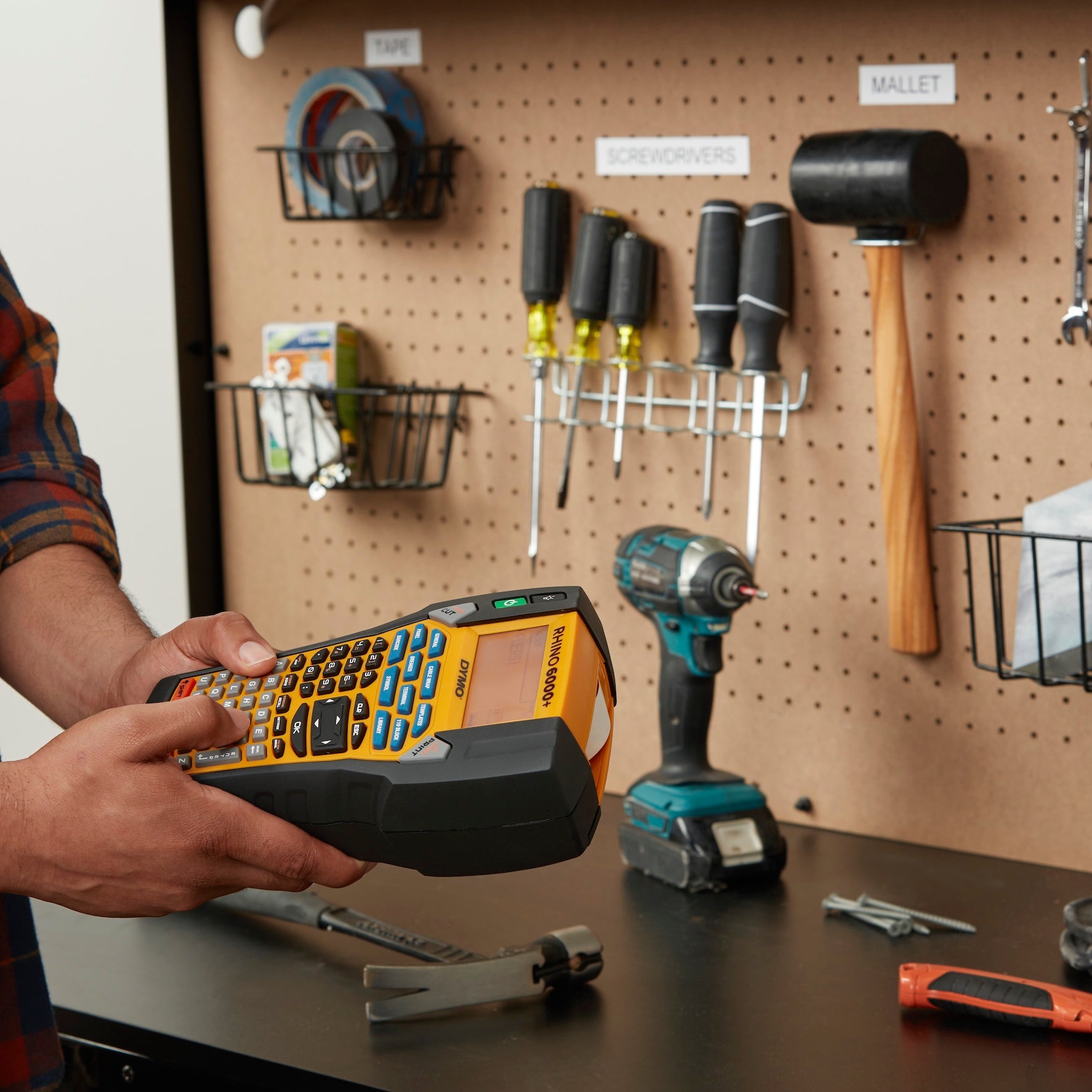 Person using a DYMO Rhino 6000 Plus label printer to organise and label tools on a workshop pegboard