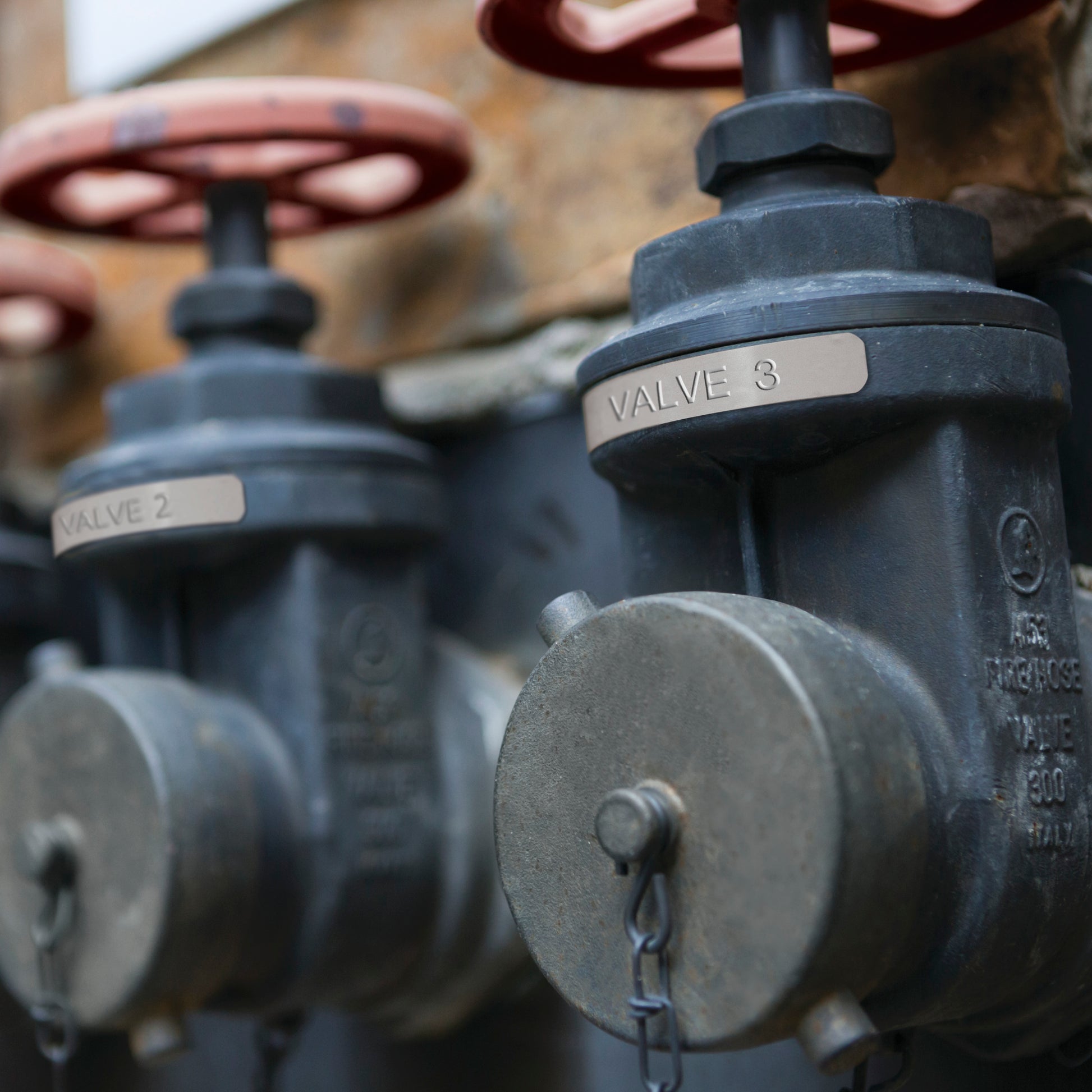 Industrial pipe valves with engraved metal identification labels marked Valve 2 and Valve 3