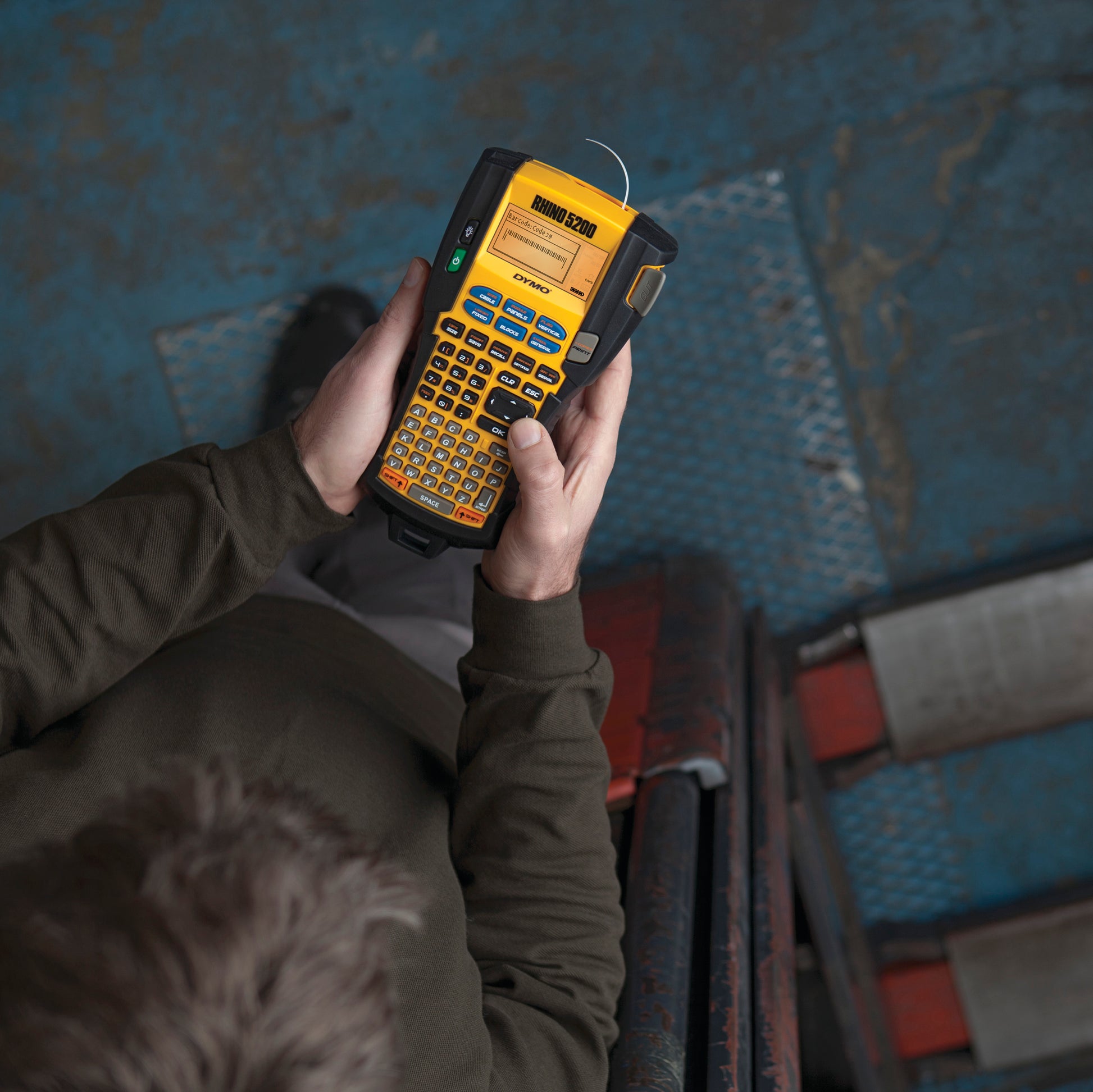 Worker holding a DYMO Rhino 5200 industrial label printer in an industrial workshop setting