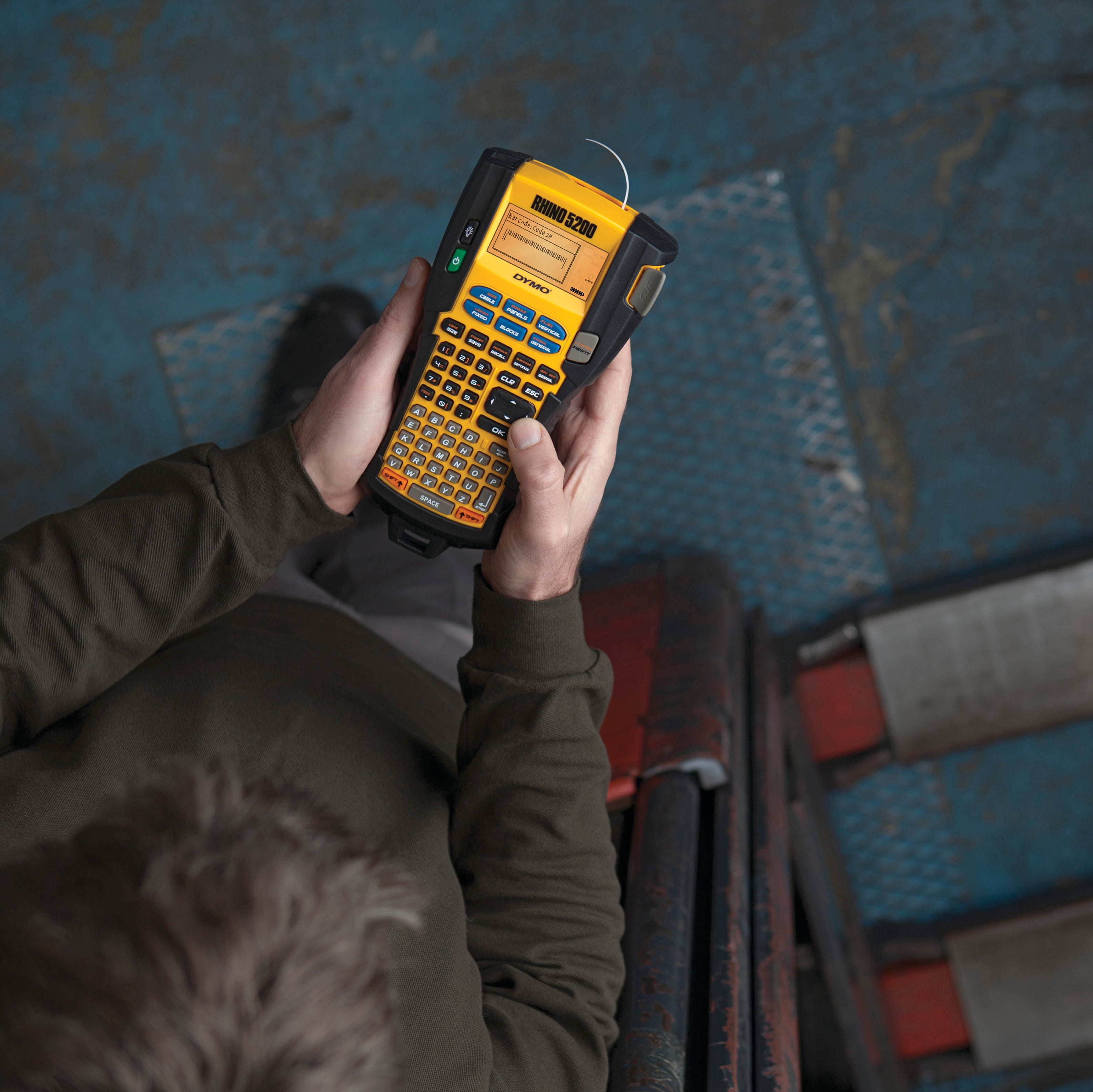 Worker holding a DYMO Rhino 5200 industrial label printer in an industrial workshop setting
