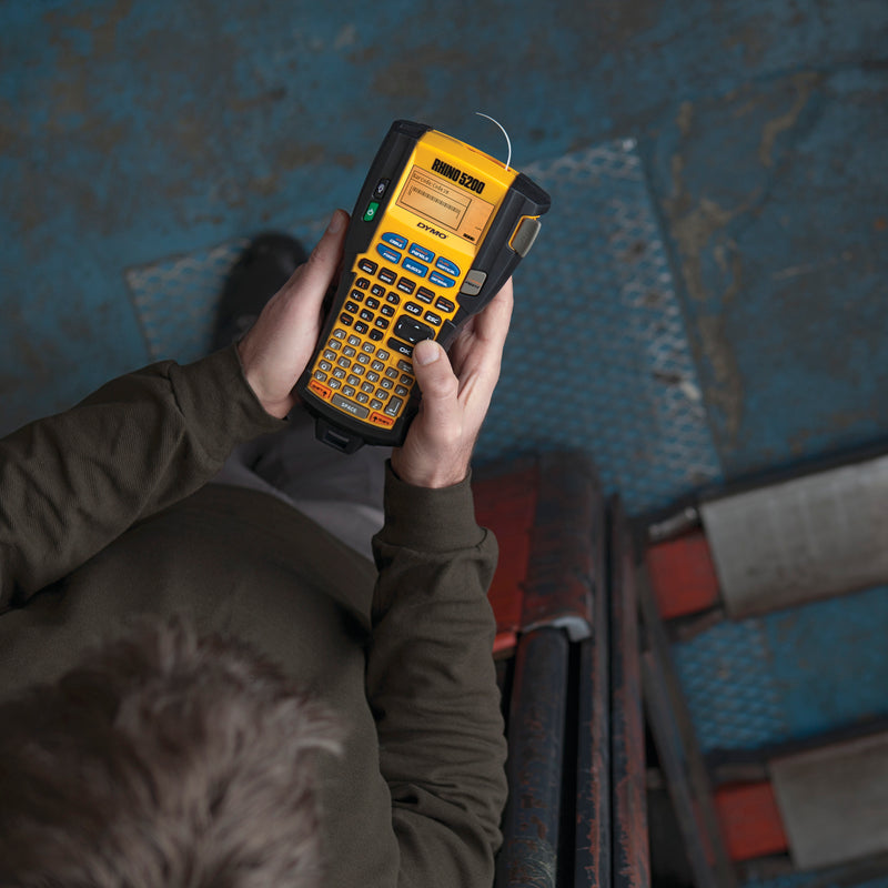 Worker holding a DYMO Rhino 5200 industrial label printer in an industrial workshop setting
