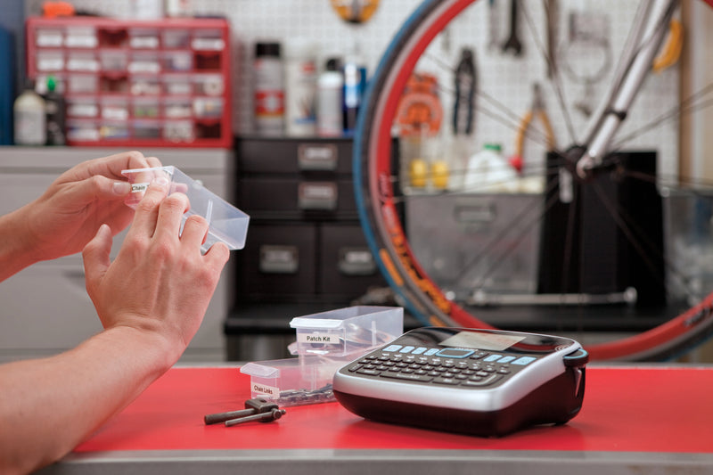 Person organising labelled parts bins with a DYMO label maker on a bicycle workshop bench
