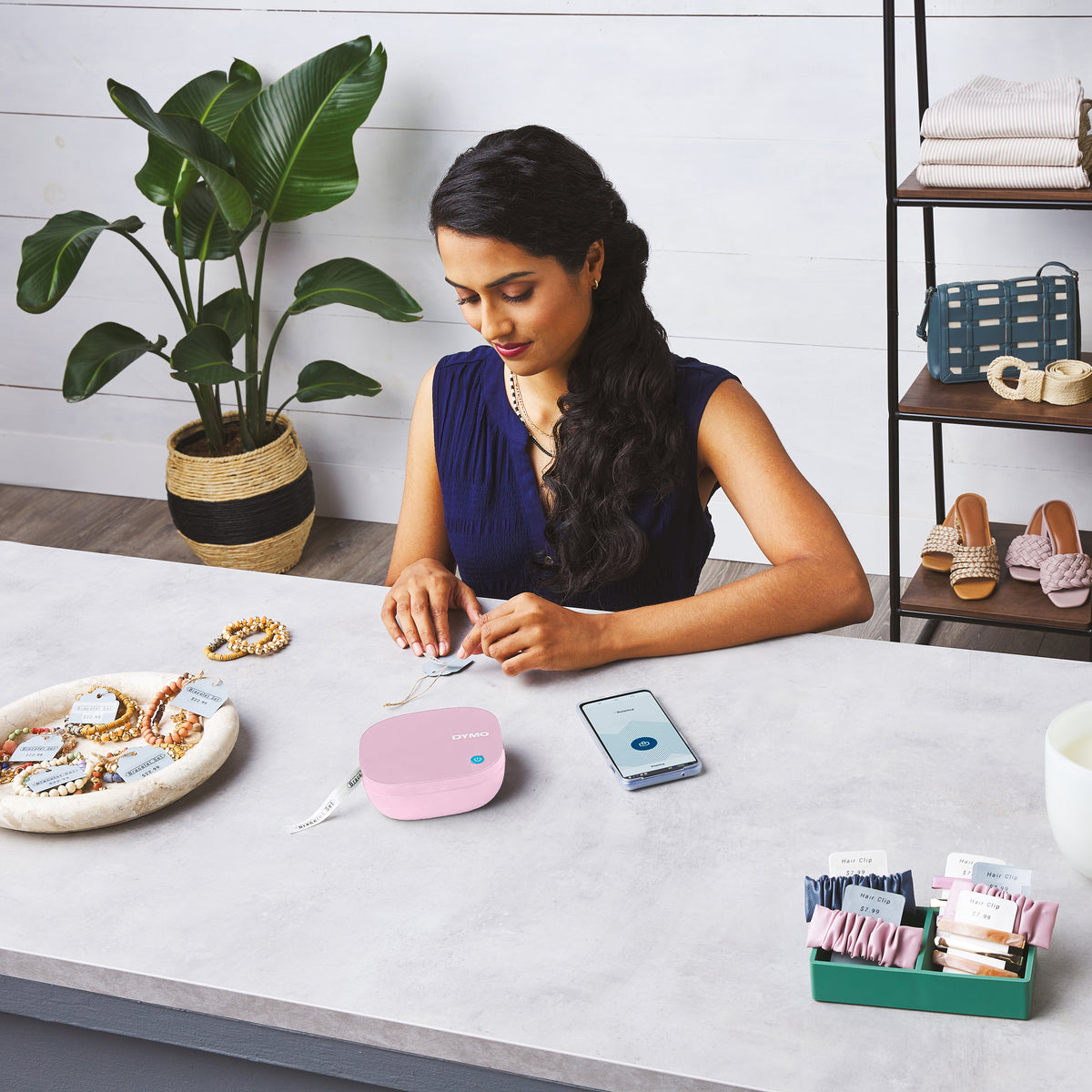 Person making labels with a pink LetraTag 200B and phone at a desk